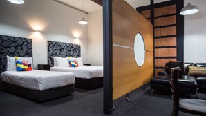 A hotel room with two beds, a wooden partition, a mirror, and a seating area with a chair and a table.