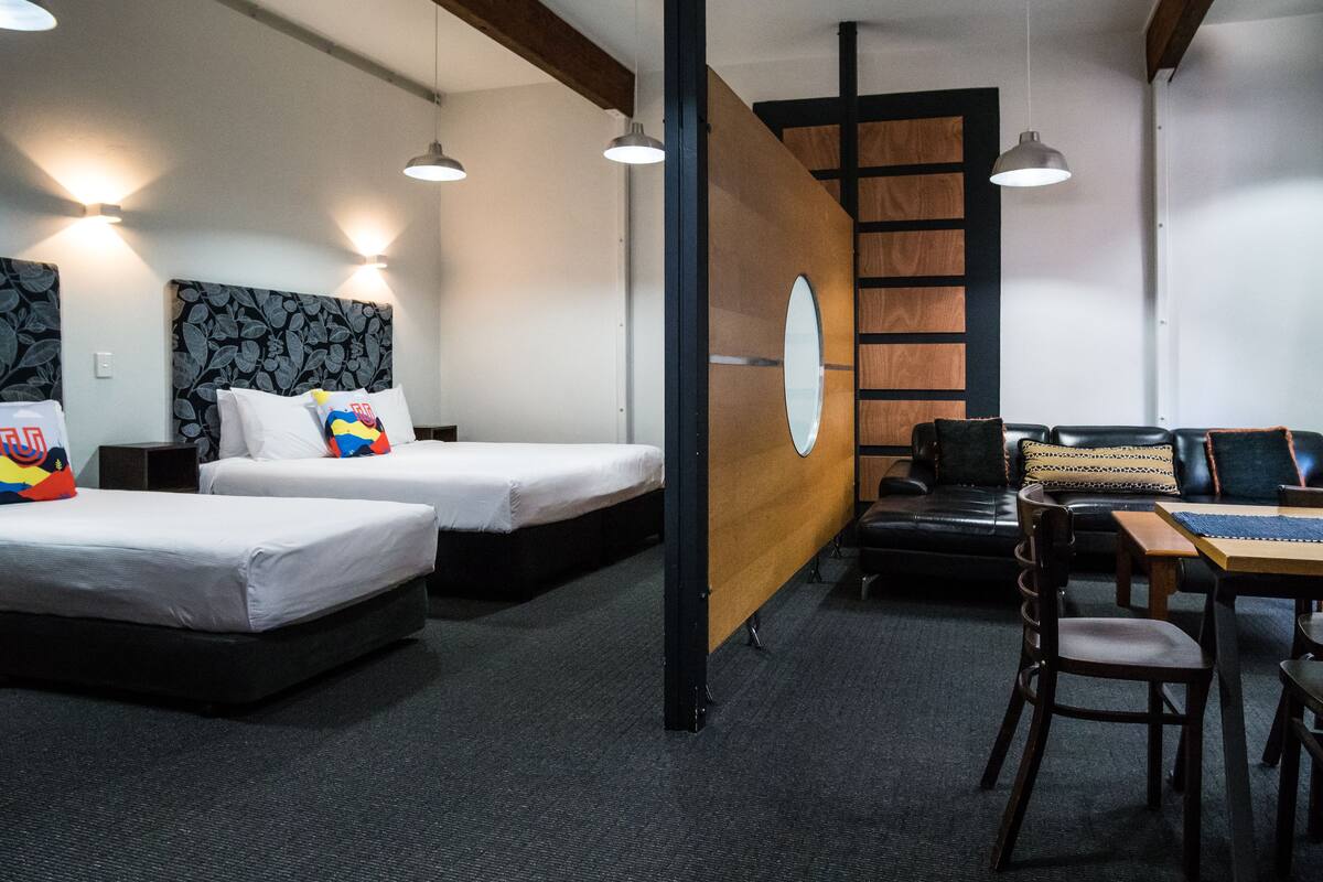 A hotel room with two beds, a sofa, a table, and a desk.