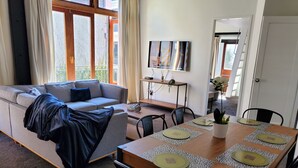 A living room with a sofa, a dining table with placemats, and a TV on the wall.
