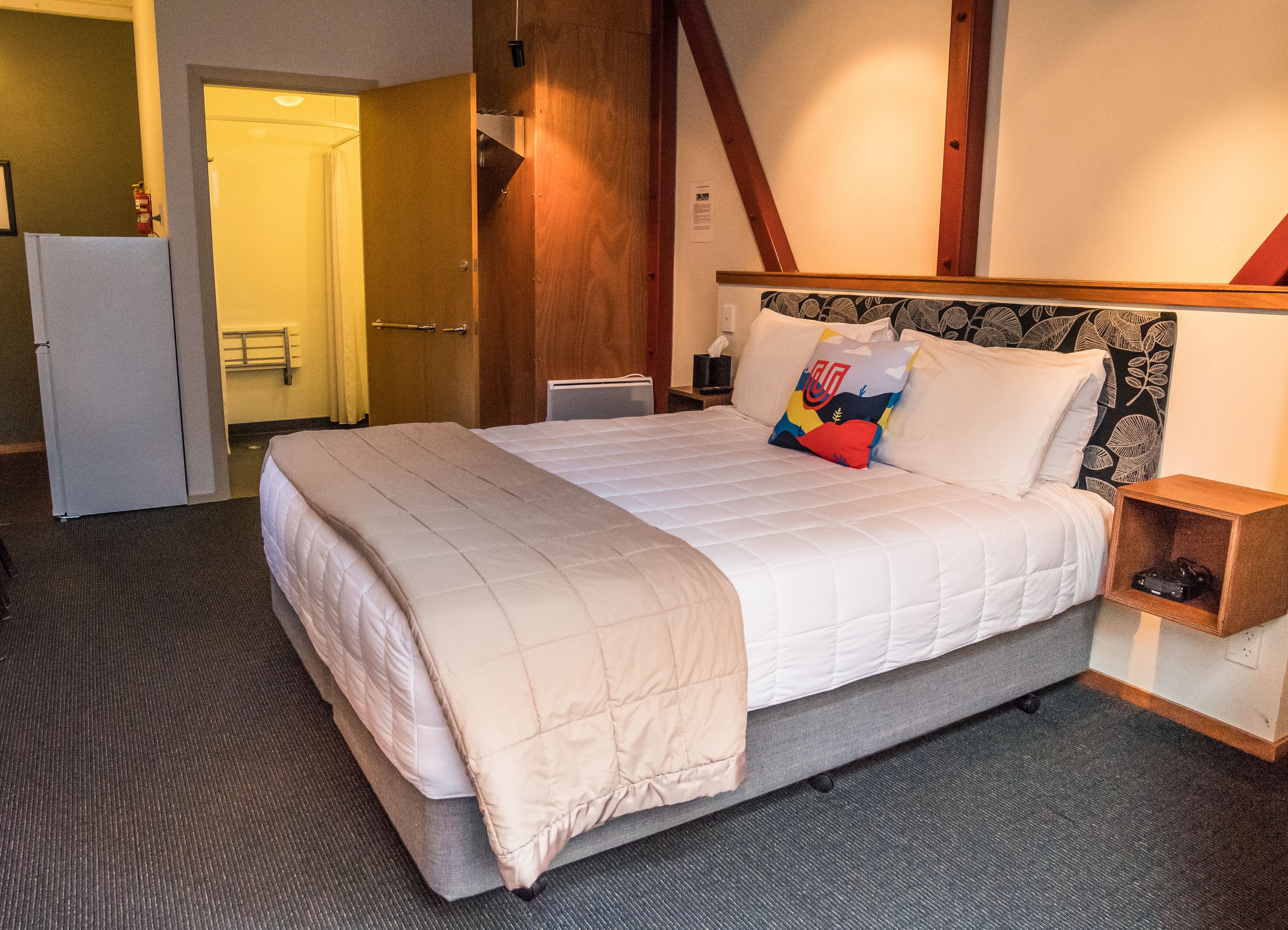 A hotel room with a large bed, a bedside table, a nightstand, a wardrobe, and a bathroom visible through an open door.