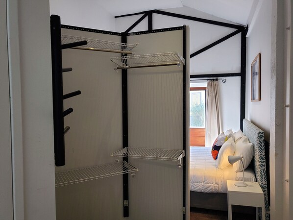 A bedroom with a bed, a bedside table with a lamp, and a wardrobe with metal shelves.