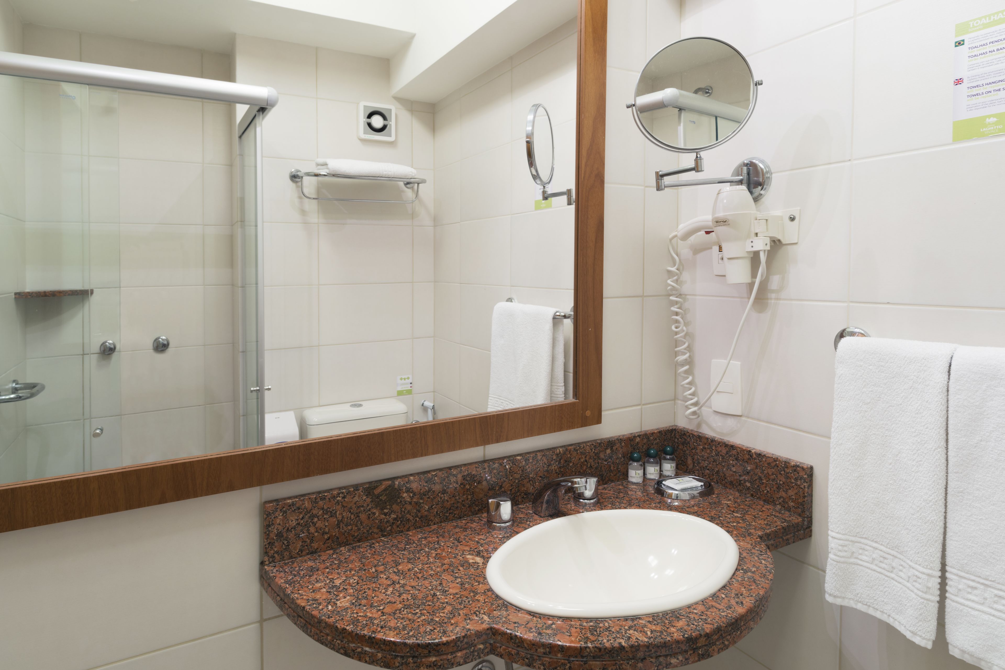 Un baño con lavamanos de encimera de granito, un espejo, toallero y cabina de ducha de vidrio.