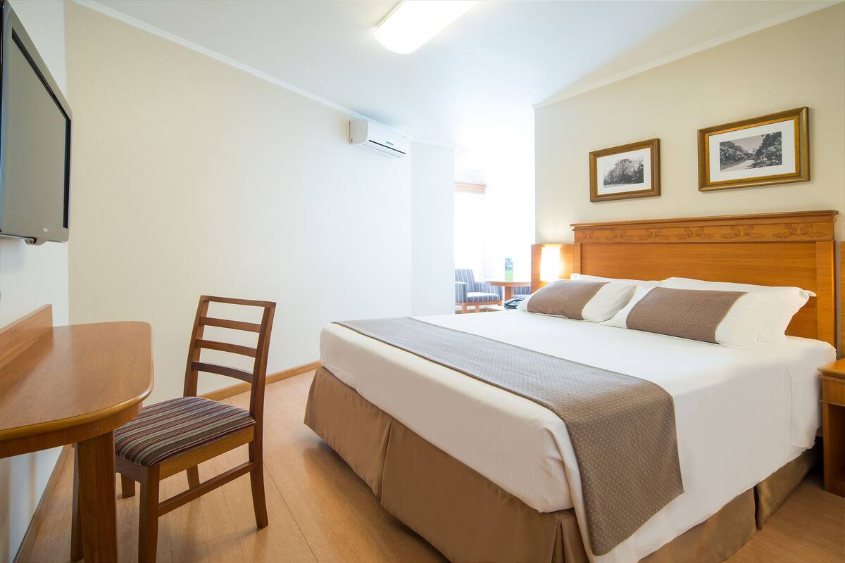 Ett hotellrum med en säng, en stol, ett bord och två inramade tavlor på väggen.