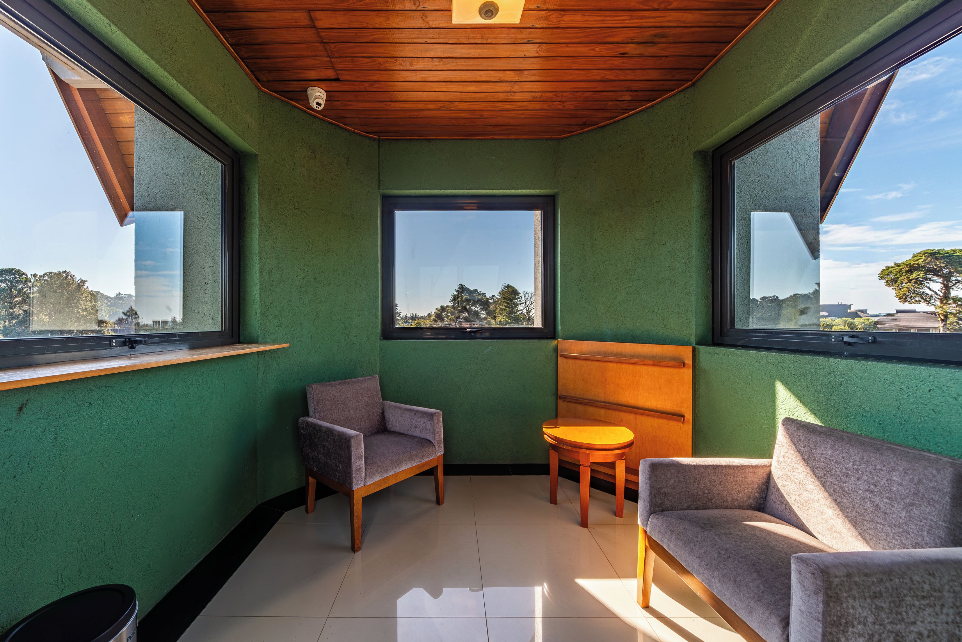 Quarto de canto com teto de madeira, janela e duas cadeiras.