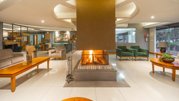 A spacious living area with a central fireplace, modern furniture, and a view of the outdoors. - Hotel Laghetto Premio (Gramado)