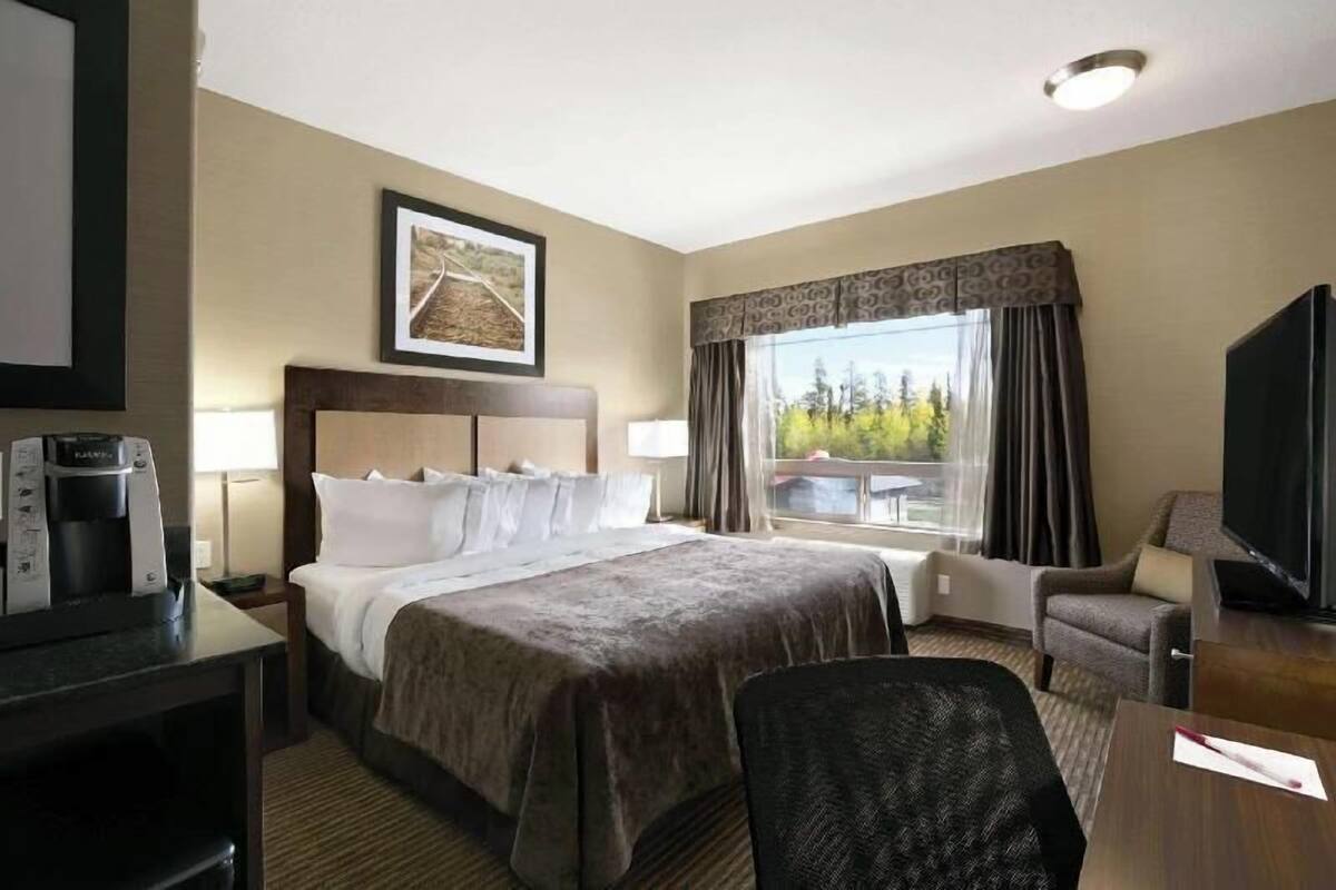 A hotel room with a large bed, a desk with a coffee maker, a TV, and a window with curtains.