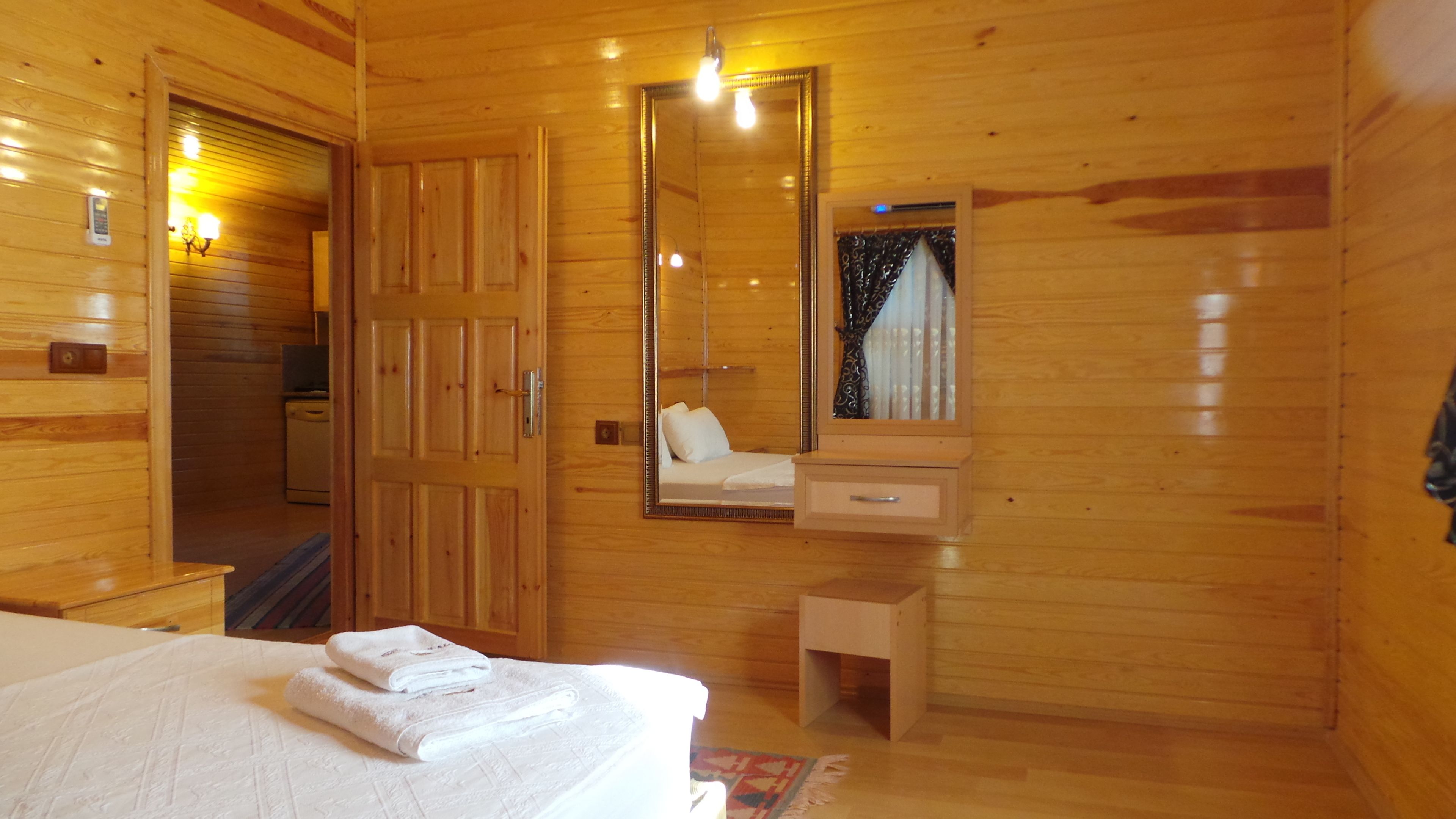 A wooden cabin room with a bed, a dresser, a mirror, and a small cabinet.