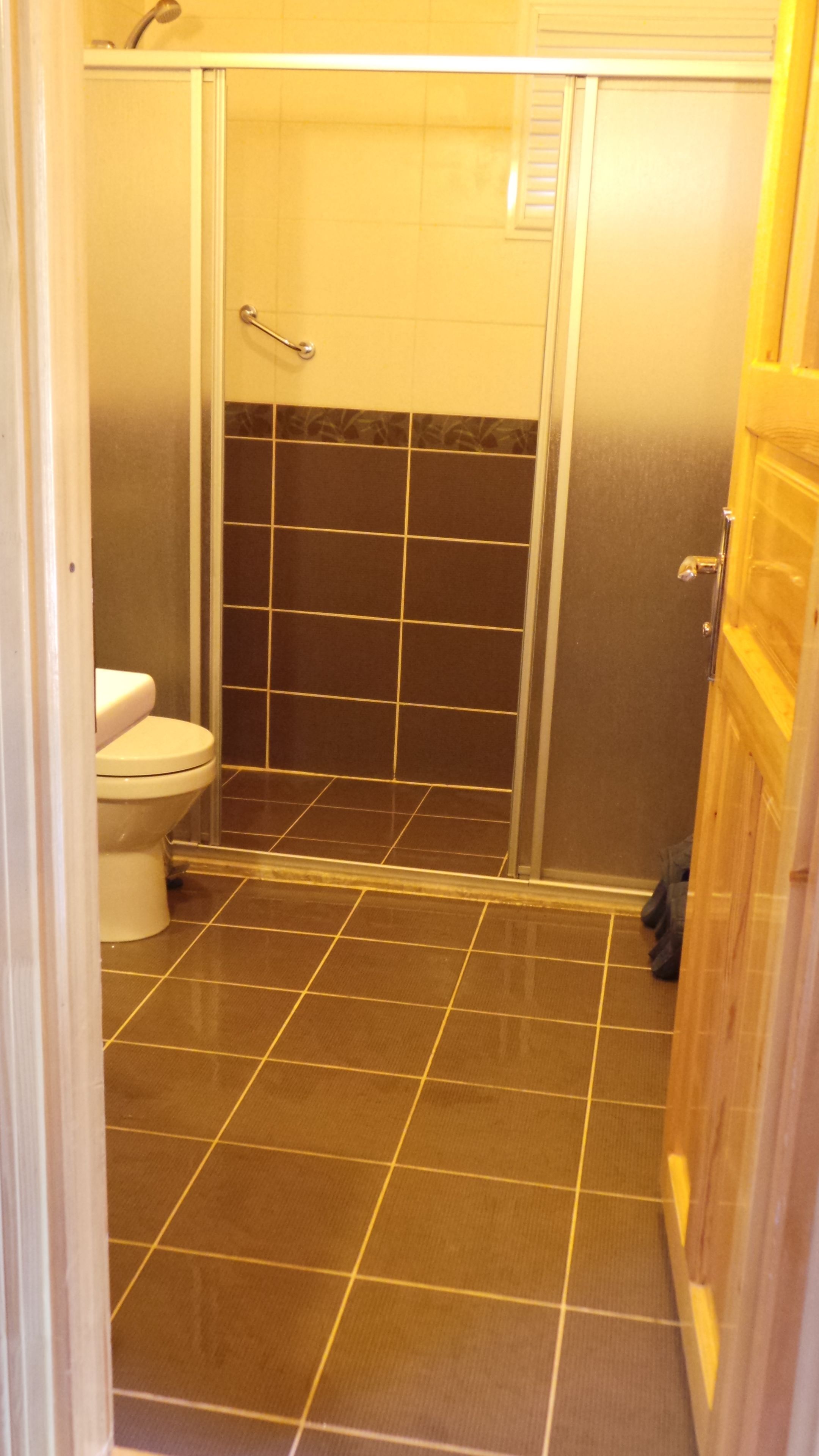 Un baño con ducha, inodoro y suelo de baldosas.