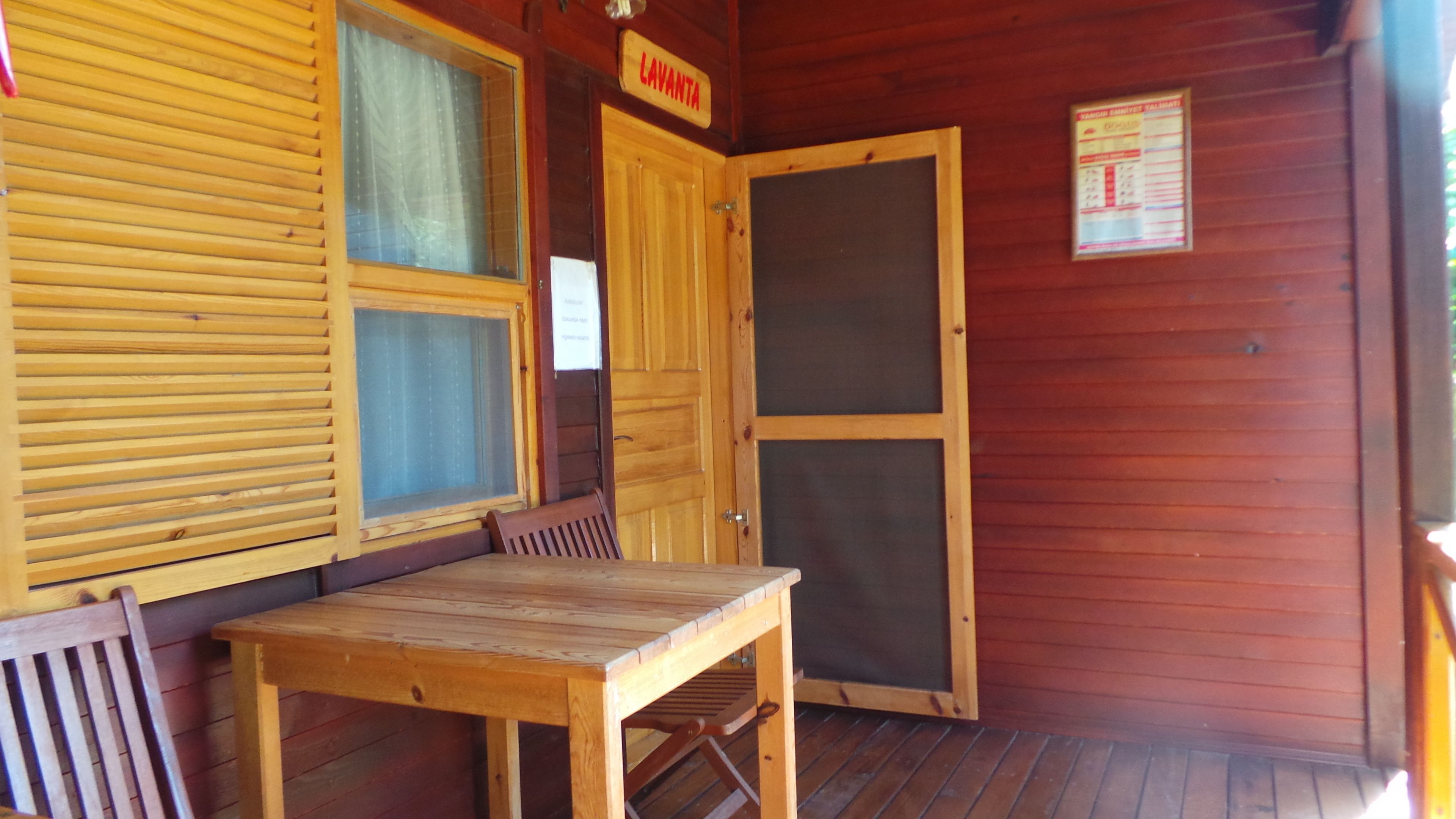 A wooden cabin with a wooden table and bench, a door labeled "LAVANTA", and a window with blinds.
