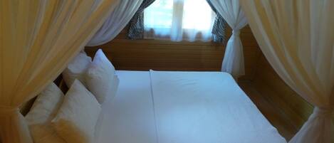 Una cama con sábanas y almohadas blancas, cubierta con cortinas traslúcidas.