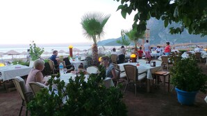 Un área de comedor al aire libre con mesas y sillas, con vista a una playa y al mar.