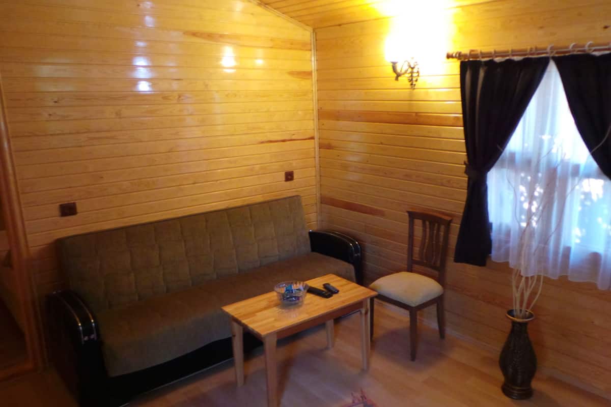 Un intérieur en bois avec un canapé, une petite table, une chaise et une fenêtre avec des rideaux.