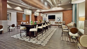 A modern dining area with a long table, chairs, and a TV mounted on the wall. - Hampton Inn & Suites Chapel Hill-Carrboro/Downtown (Carrboro)