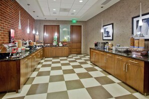 A hotel kitchen with checkered flooring, wooden cabinets, and various kitchen appliances. - Hampton Inn & Suites Chapel Hill-Carrboro/Downtown (Carrboro)