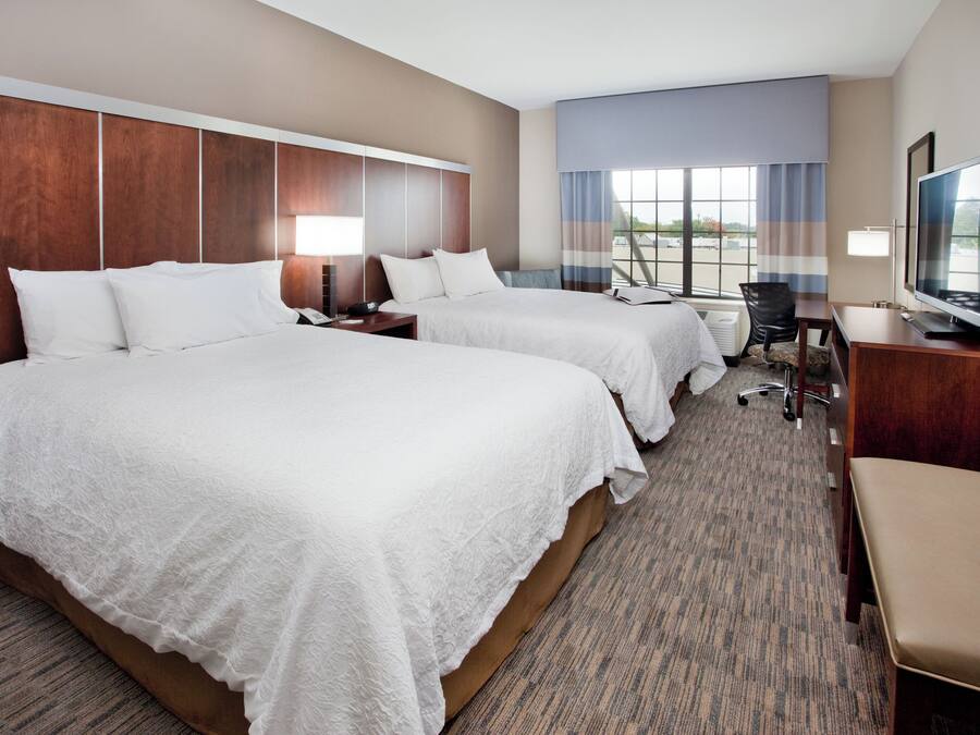 A hotel room with two beds, a desk, a chair, a television, and a large window.