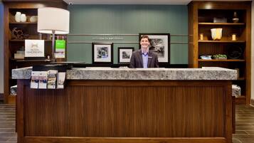 A hotel reception desk with a wooden panel design, a large marble counter, and framed pictures on the wall.