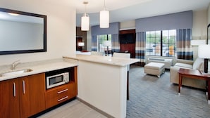 A hotel room with a kitchenette, a large mirror, a flat-screen TV, a sofa, and a dining table. - Hampton Inn & Suites Chapel Hill-Carrboro/Downtown (Carrboro)