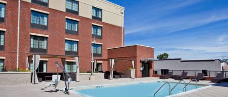 A swimming pool with a covered seating area and a brick building in the background.