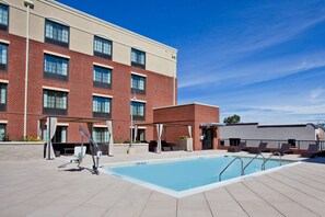 A swimming pool with a covered seating area and a brick building in the background. - Hampton Inn & Suites Chapel Hill-Carrboro/Downtown (Carrboro)