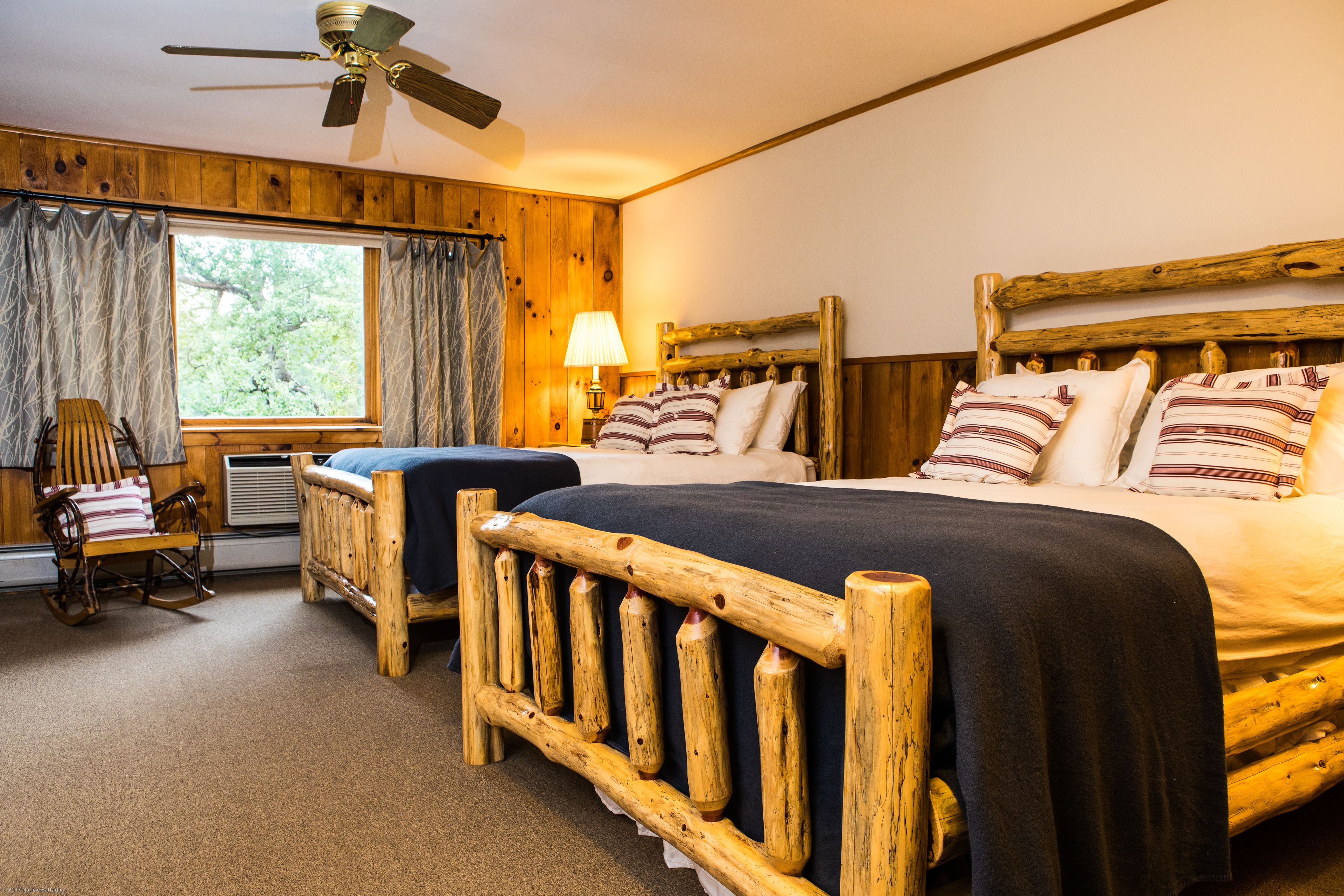 A wooden-framed bedroom with two beds, a rocking chair, and a ceiling fan.