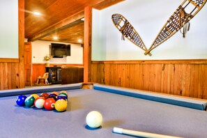 A pool table with balls and a cue stick, wooden walls, and a heart-shaped decoration on the wall.