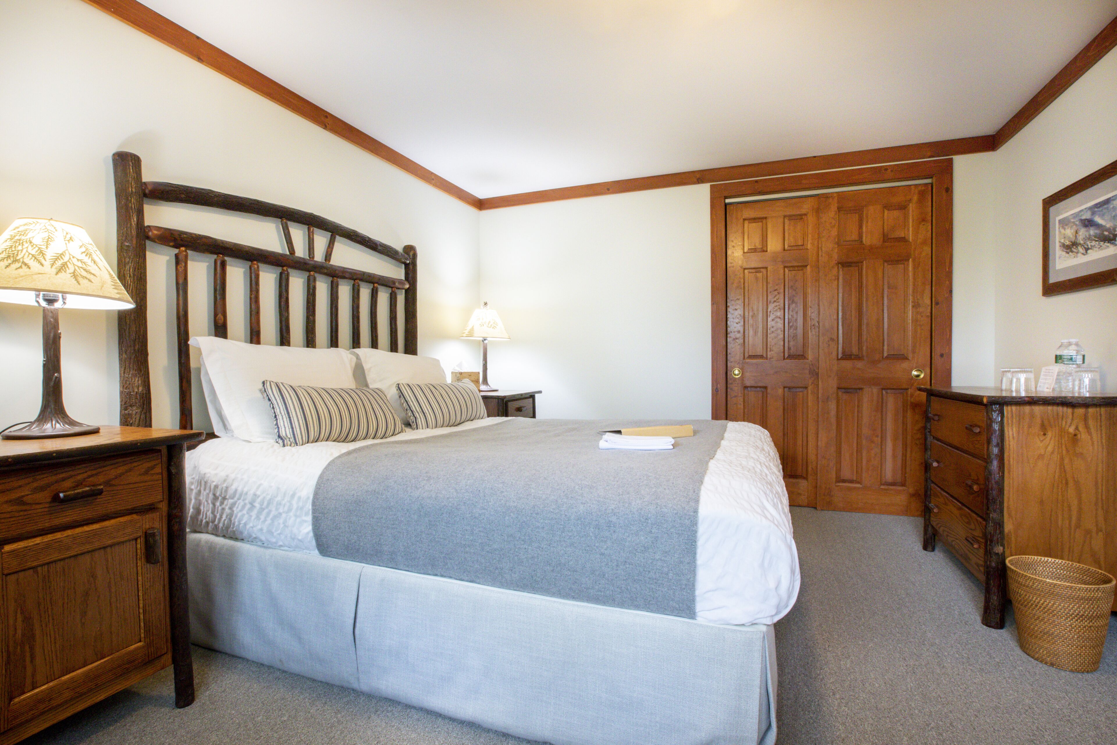 Un dormitorio con una cama de madera, dos mesitas de noche con lámparas, un aparador de madera y una puerta.