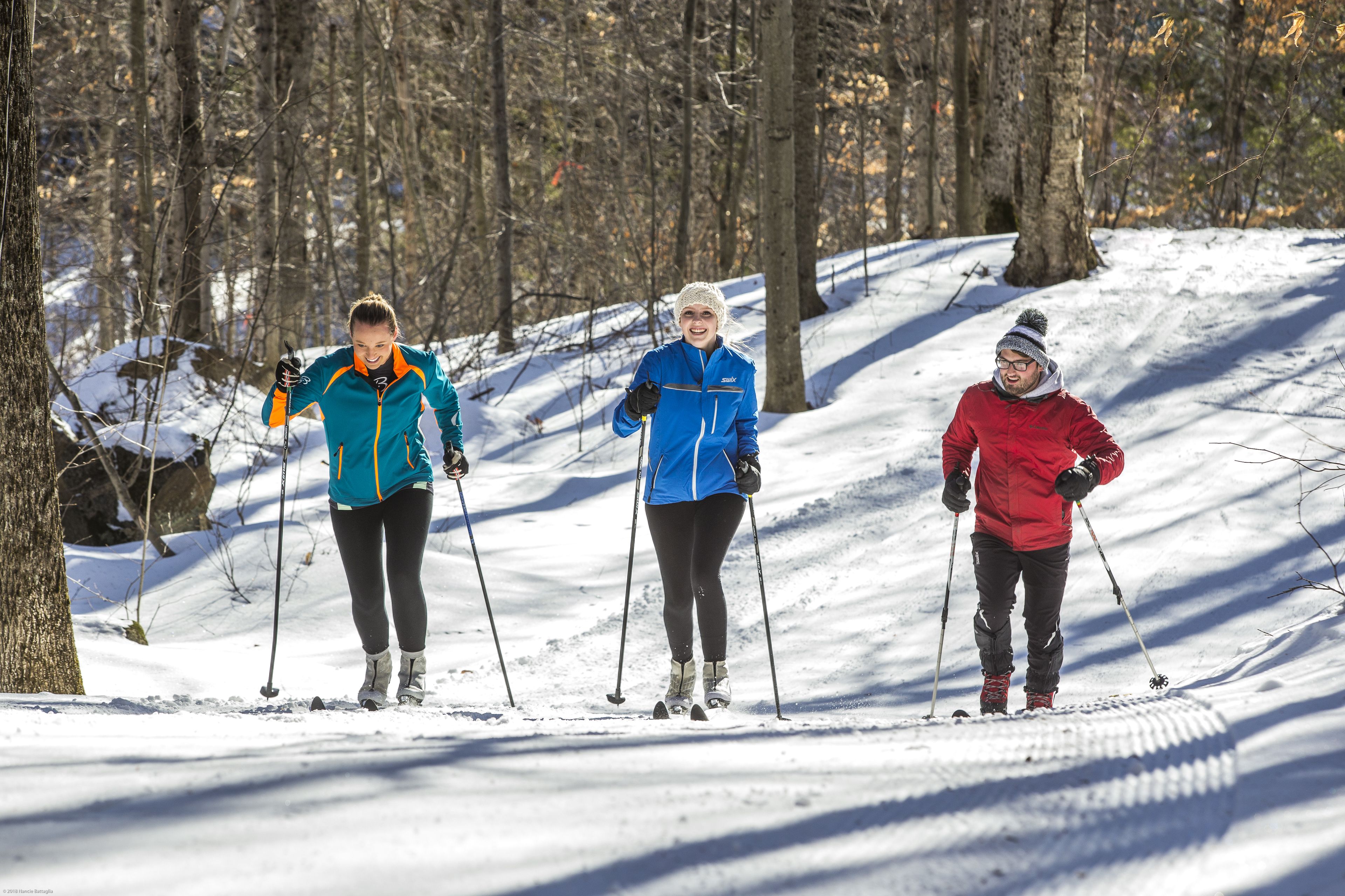 Three people cross-country skiing on a snowy trail surrounded by trees.