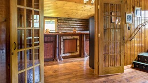 Un interior de madera con un gran ventanal abierto que da a una zona de cocina, una escalera y un piso de madera.