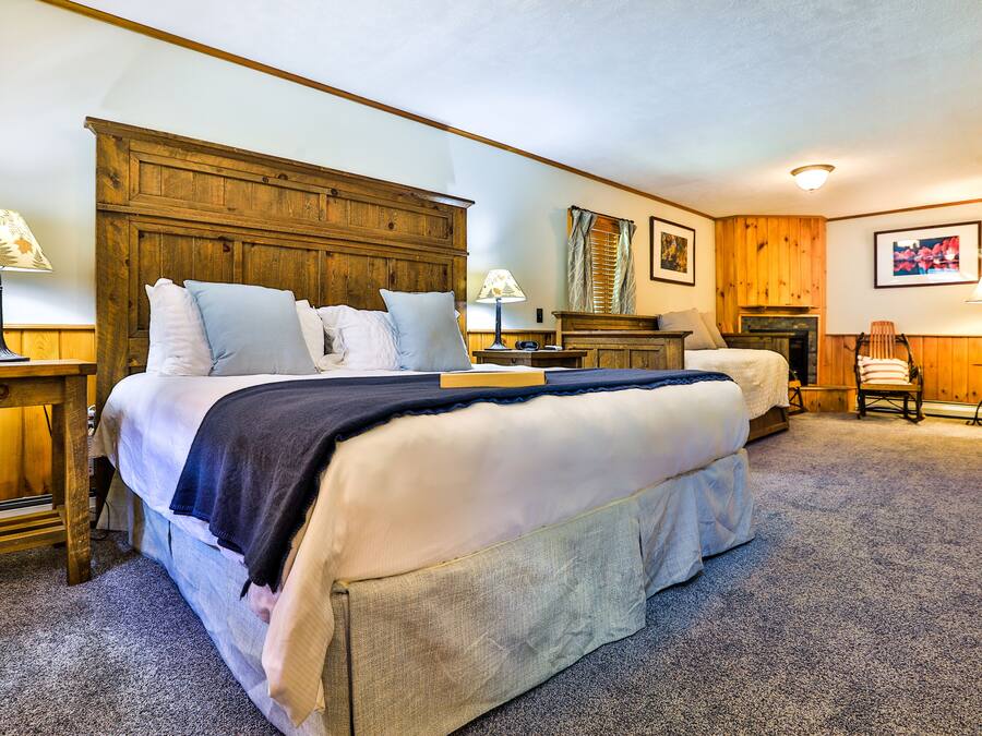 A bedroom with a large bed, a wooden headboard, two bedside tables with lamps, a chair, and a fireplace.