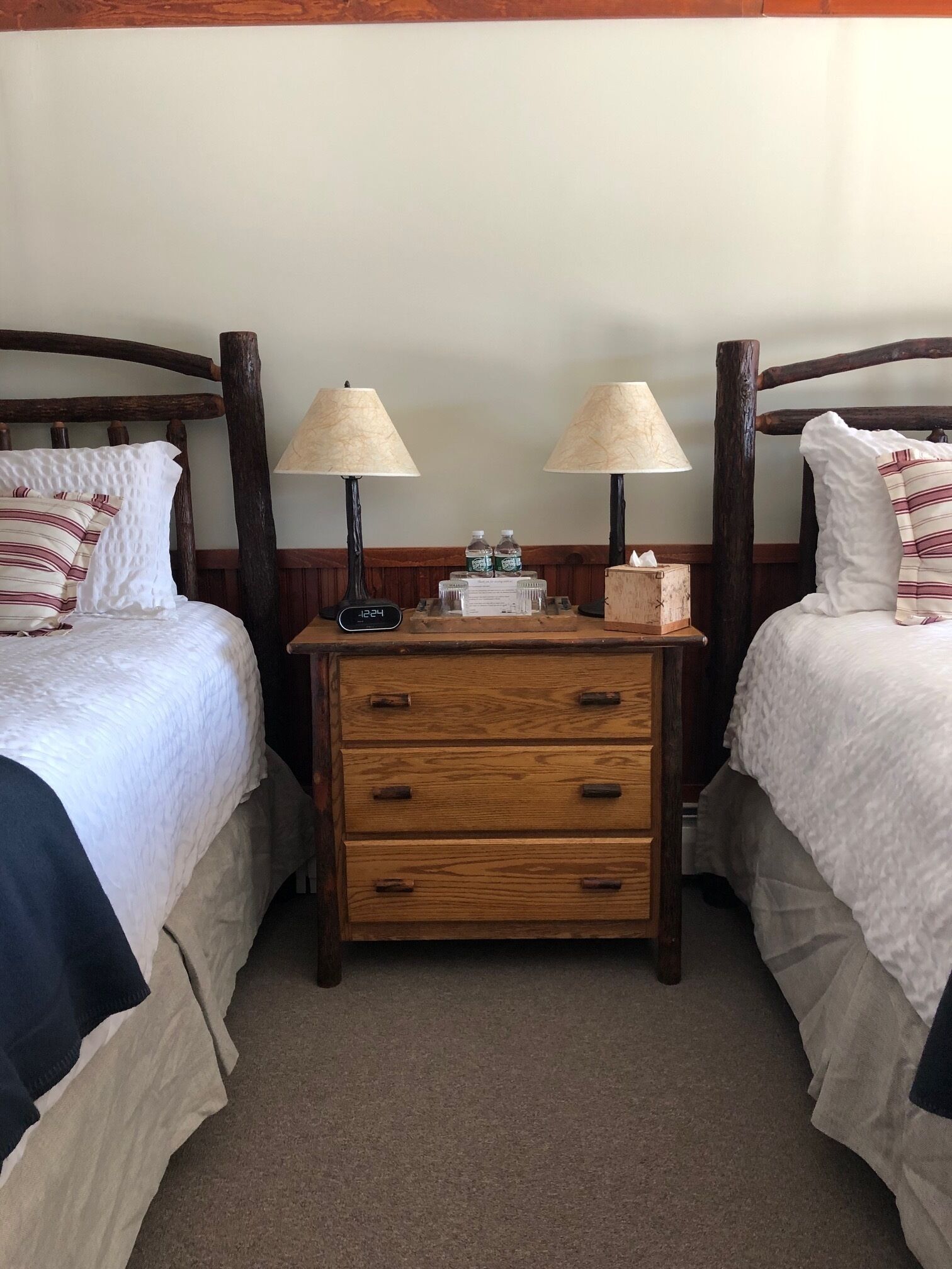 Een tweepersoonskamer met twee bedden, houten nachtkastjes met lampen en een kleine houten dressoir.