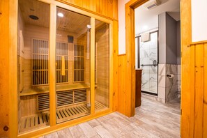 A sauna with wooden walls and a glass door, a shower area with marble tiles, and a wooden floor.