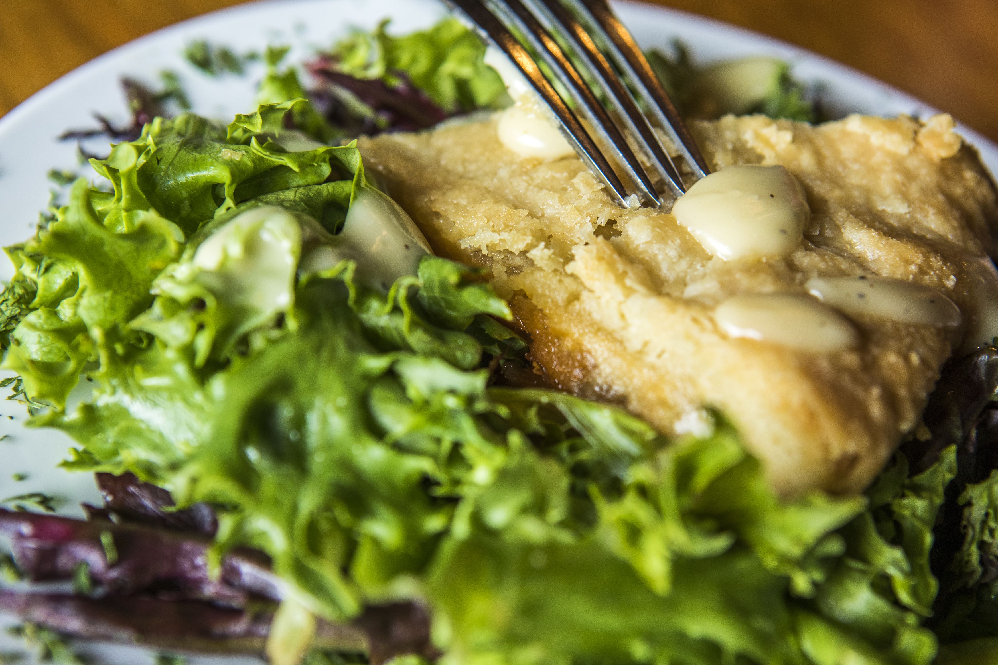 A plate with a piece of fish, salad, and a fork.