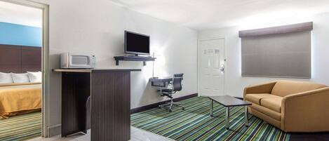 A hotel room with a bed, a desk with a computer, a television, a couch, and a striped carpet.
