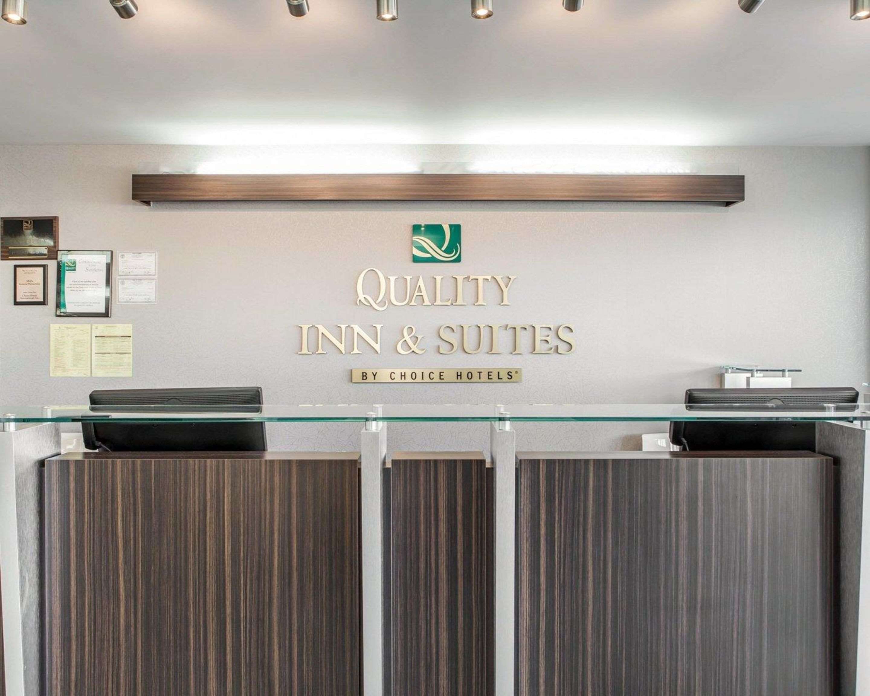 A reception desk with a glass top, framed certificates on the wall, and a sign reading "Quality Inn & Suites by Choice Hotels".