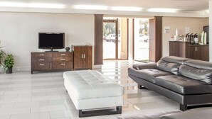 A modern living room with a flat-screen TV, a dark wooden cabinet, a white ottoman, and a dark leather sofa. - Quality Inn & Suites Jasper - Kimball (Jasper)