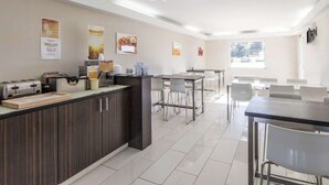 A modern kitchen with a central island, a dining area with tables and chairs, and a view of the outdoors through a large window. - Quality Inn & Suites Jasper - Kimball (Jasper)