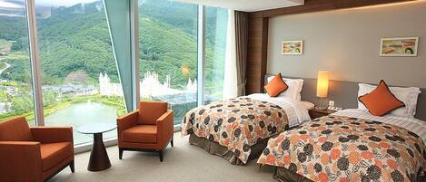 Habitación de hotel con dos camas, una mesita, dos sillones y grandes ventanales con vistas a un castillo y vegetación.