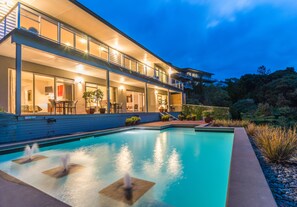 A modern house with a swimming pool, outdoor seating, and a well-lit balcony. - Decks of Paihia (Paihia)