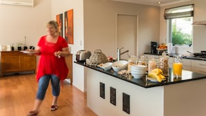 A modern kitchen with a central island, various food items, and a person in a red dress. - Decks of Paihia (Paihia)