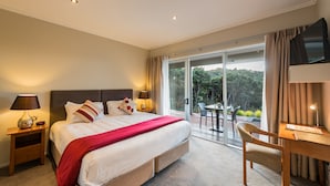 A hotel room with a large bed, a desk, a chair, and a view of the outdoors. - Decks of Paihia (Paihia)