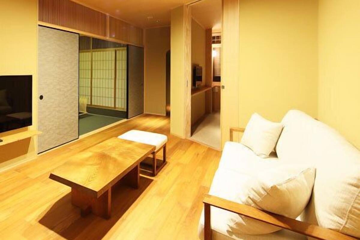 Une pièce avec un plancher en bois, un canapé, une table et une porte coulissante qui donne sur une autre pièce.