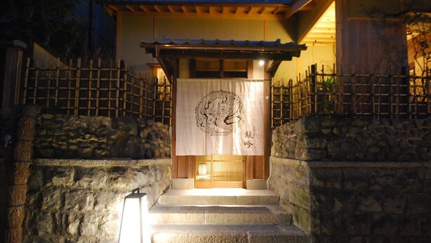 A traditional Japanese building with stone steps leading to a wooden entrance, a lantern on the steps, and a decorative hanging at the entrance. - Ishibekoji Ryugin (Kyoto)