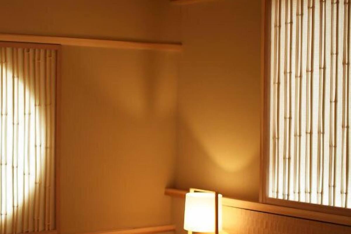 Une chambre d’hôtel avec un lit, une table de chevet avec une lampe et une fenêtre avec des stores verticaux.