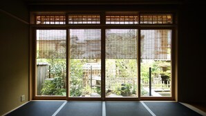 A room with tatami mat flooring and a sliding shoji screen door leading to a garden with various plants and a small pond. - Ishibekoji Ryugin (Kyoto)
