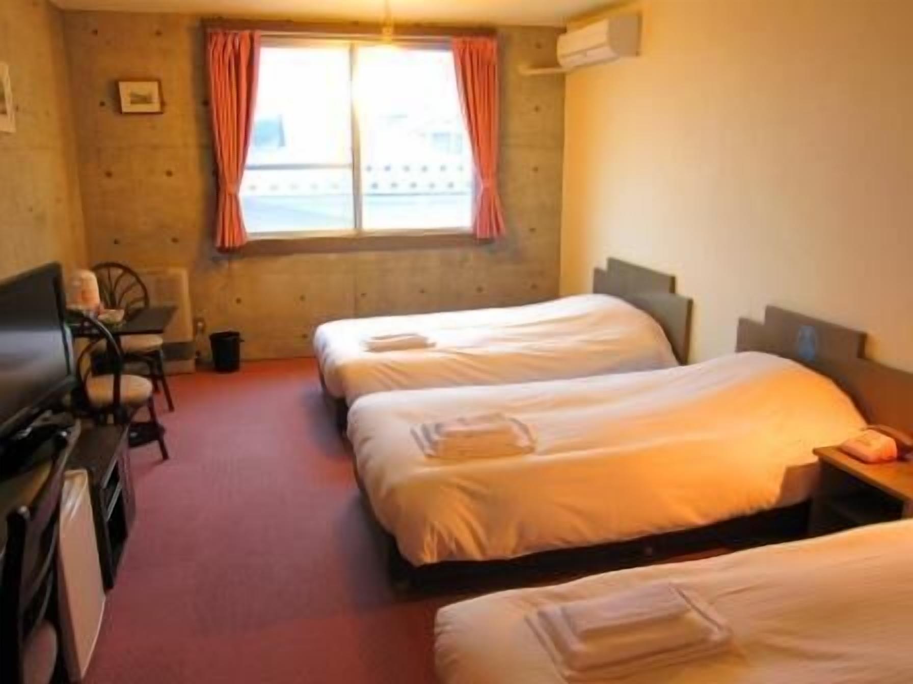 Quarto de hotel com duas camas, uma escrivaninha, uma cadeira e uma janela com cortinas.