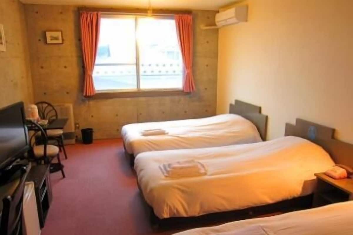 A hotel room with two beds, a desk, a chair, and a window with curtains.