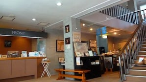 A reception area with a counter labeled "FRONT," a staircase, and framed pictures on the walls. - Hakodate Motomachi Hotel (Hakodate)