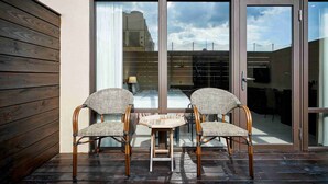 A patio with two wicker chairs and a small table, a sliding glass door, and a view of a building and sky. - CHECK Inn Taichung LaiLai (Taichung)