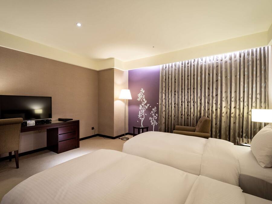 A hotel room with a large bed, a desk with a television, and a chair.