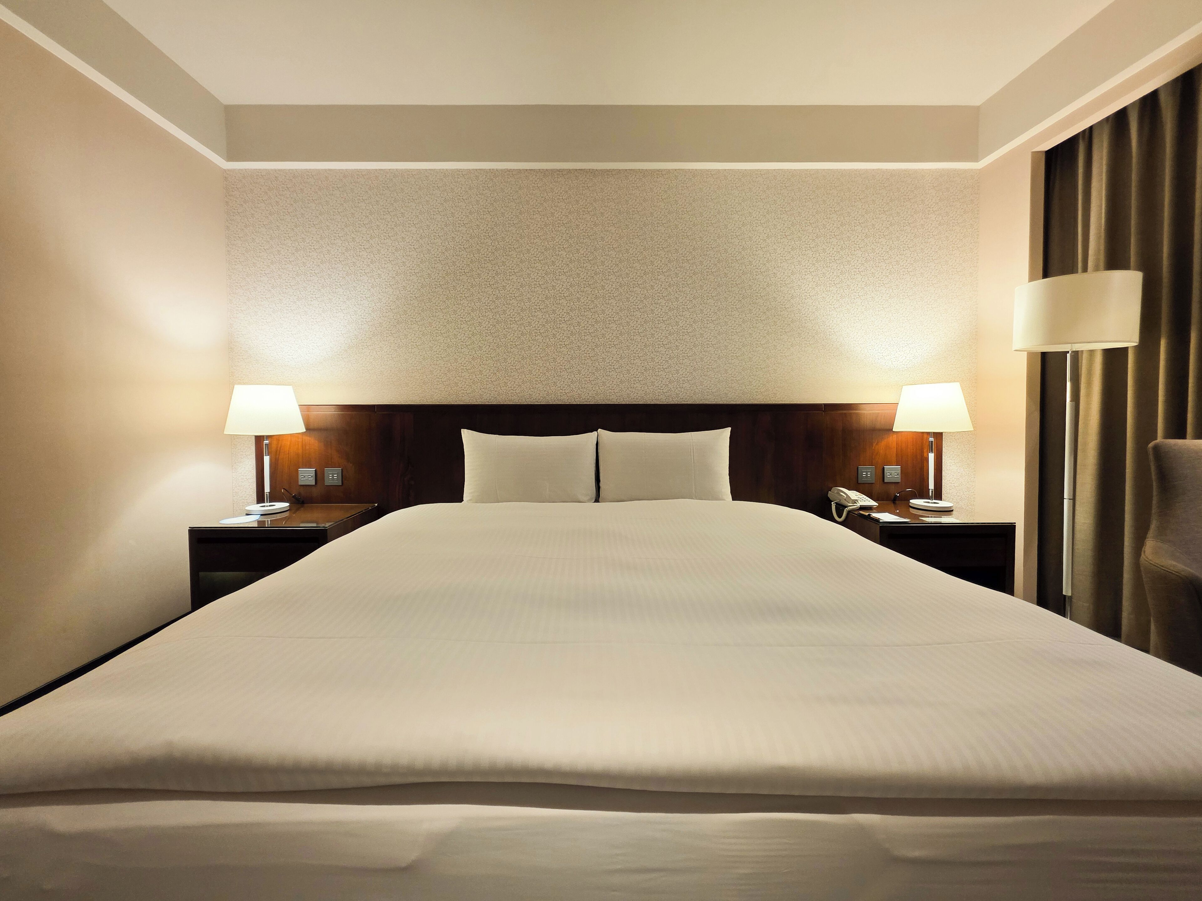 A hotel room with a large bed, two bedside tables with lamps, a telephone, and a chair.